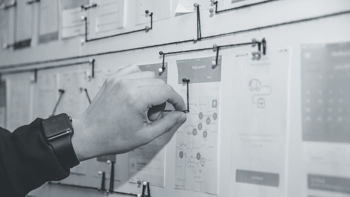 A hand pinning a user-flow diagram to a wall of screen sketches